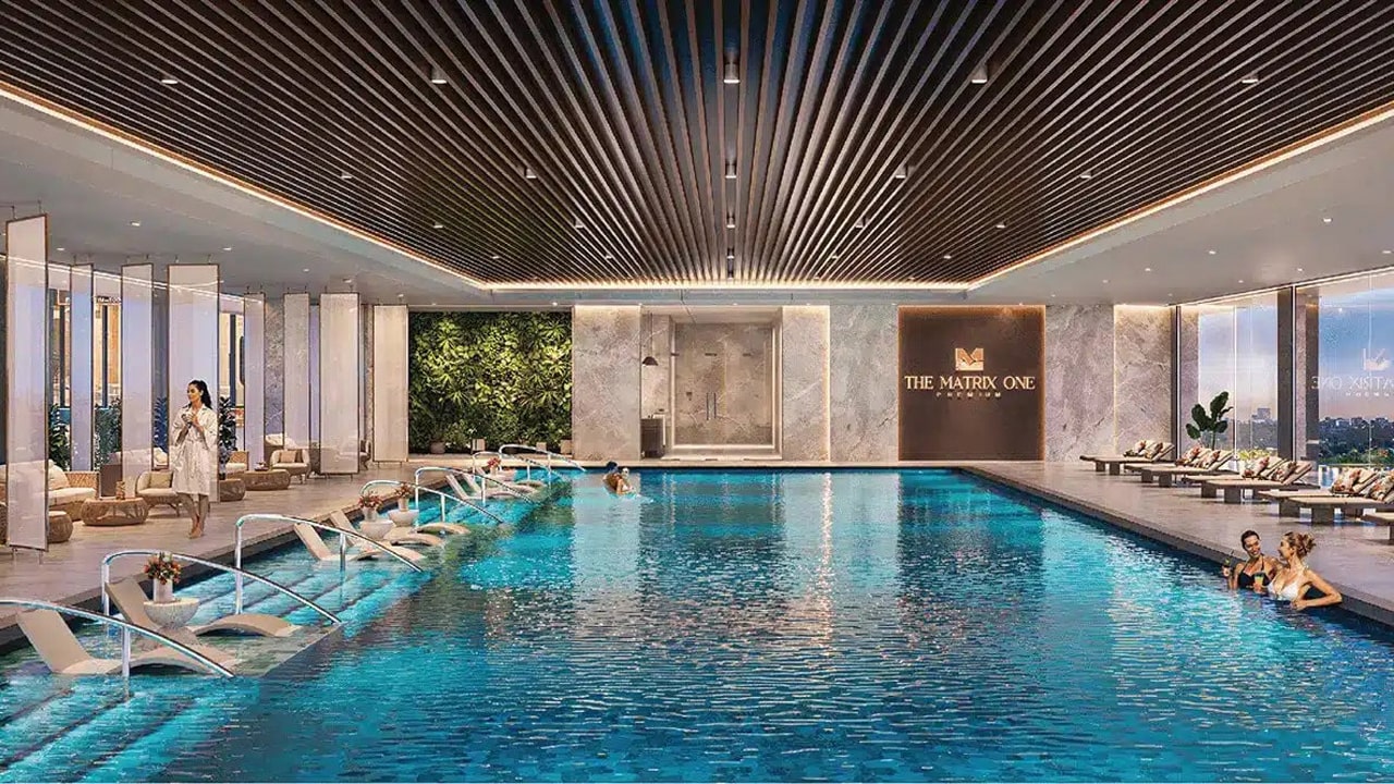 An ninh và riêng tư nhờ công nghệ 4.0 tại Vinhomes Nguyễn Trãi 19 Hình ảnh bể bơi trong nhà tại Vinhomes Nguyễn Trãi, với nước màu xanh ngọc bích, ghế ngả lưng sang trọng bên cạnh, tường cây xanh và trần gỗ tối, cùng một số cư dân thư giãn, ánh sáng tự nhiên tràn ngập qua cửa kính lớn.