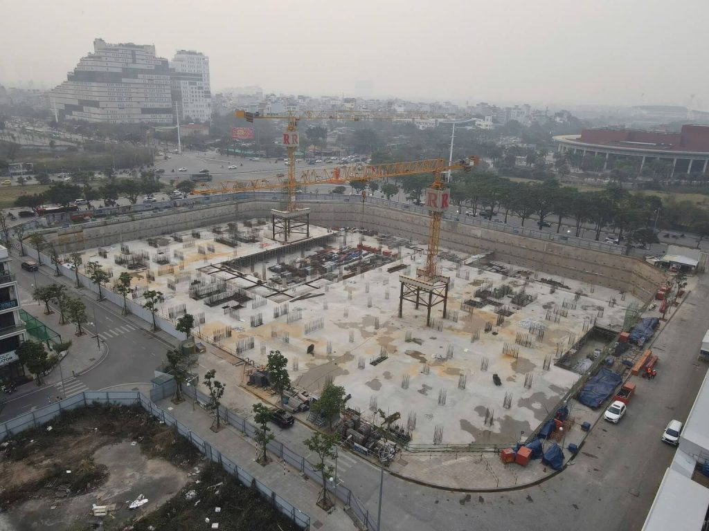 Tiến độ thi công Vinhomes Nguyễn Trãi - Cập nhật mới nhất 3 Hình ảnh từ trên cao của công trường Vinhomes Nguyễn Trãi trong giai đoạn thi công móng, với nền bê tông và vật liệu xây dựng, cùng khung cảnh thành phố Hà Nội mờ sương xung quanh.
