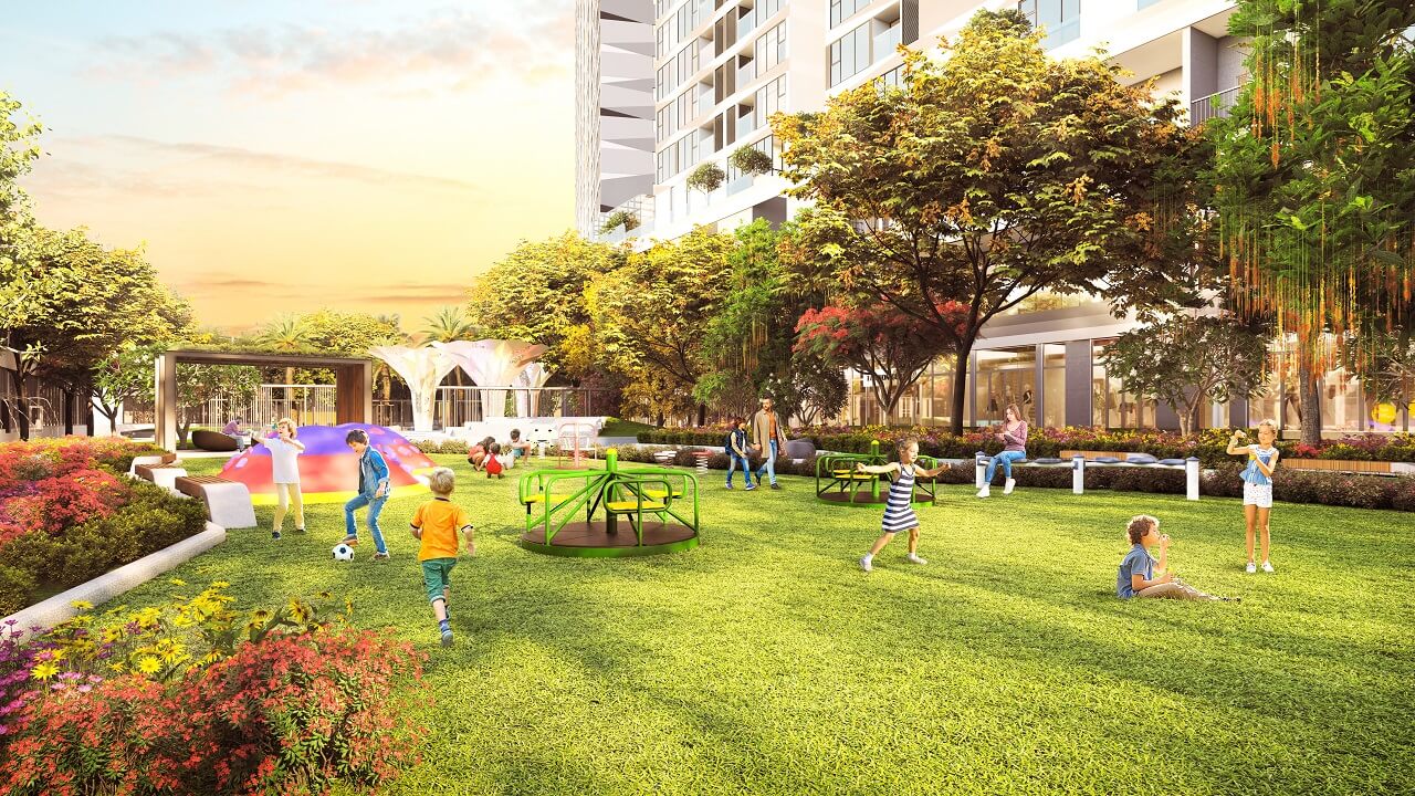 Vinhomes Nguyễn Trãi Thanh Xuân 14 Hình ảnh khu vui chơi trẻ em tại Vinhomes Nguyễn Trãi với thảm cỏ xanh, cây cối rợp bóng, các thiết bị chơi như xích đu và vòng xoay, cùng trẻ em đang vui đùa dưới ánh hoàng hôn bên tòa nhà hiện đại.